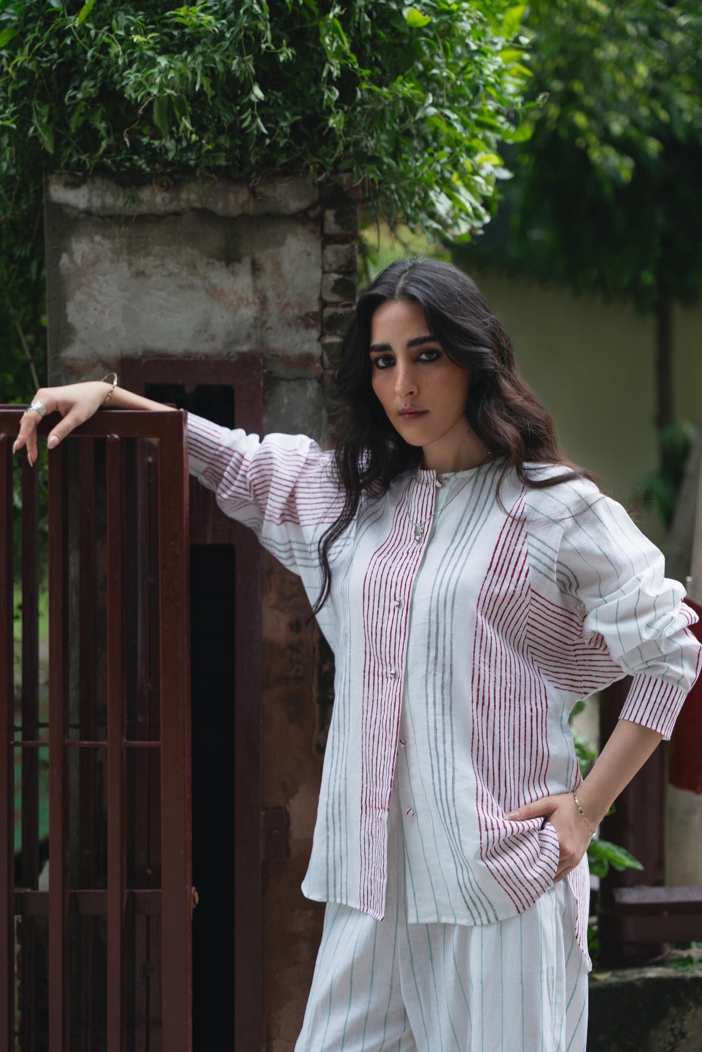 Woman in a white and red striped outfit standing outdoors with greenery in the background