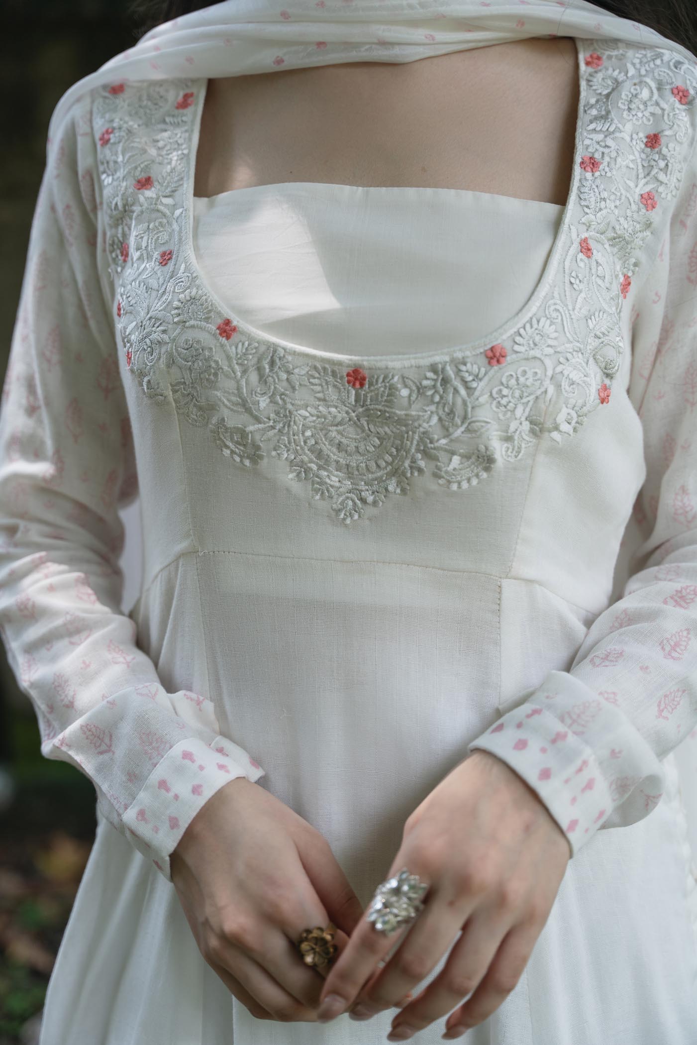 White embroidered dress with long sleeves and floral details on a blurred background