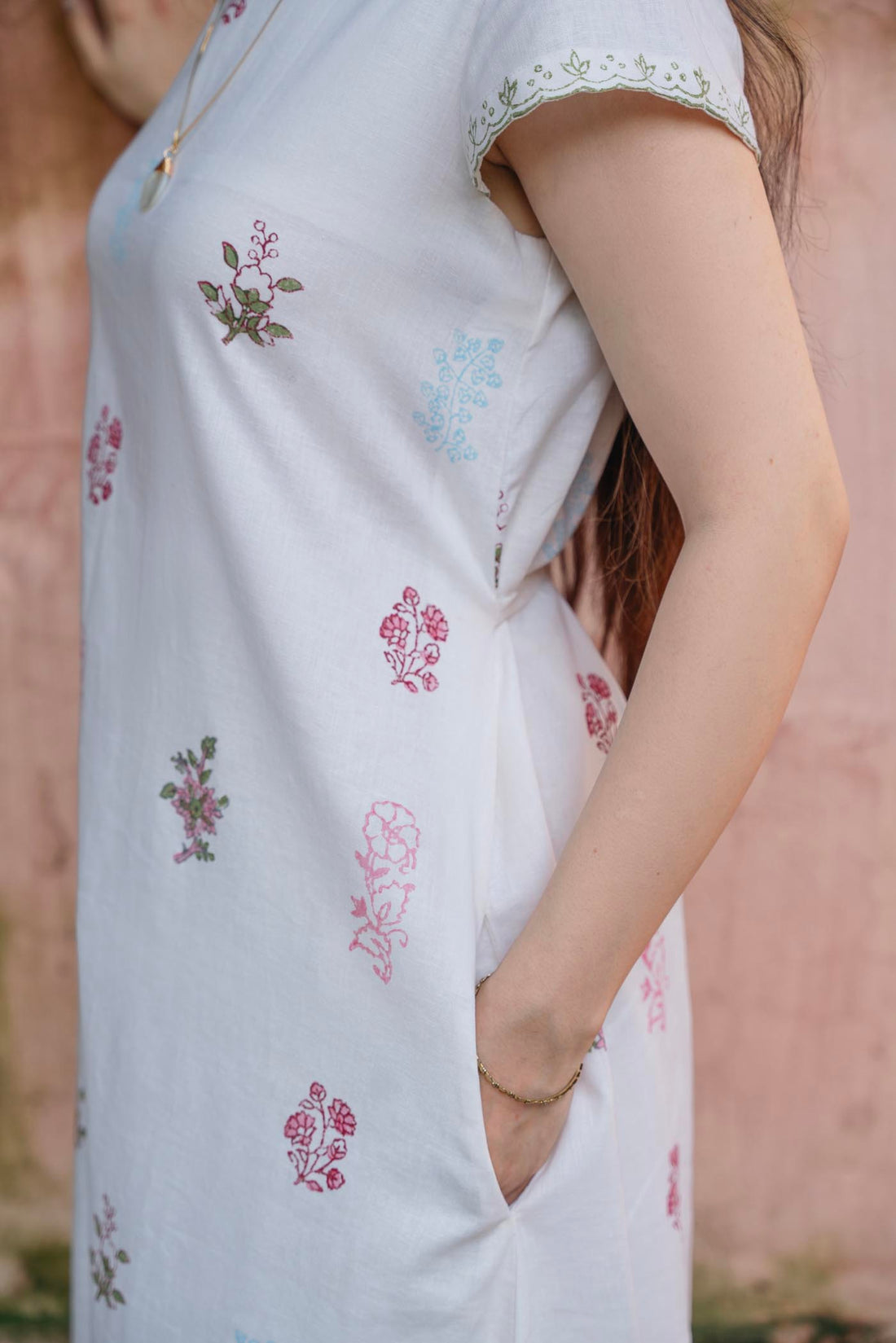 Woman in a white floral dress standing against a textured wall.