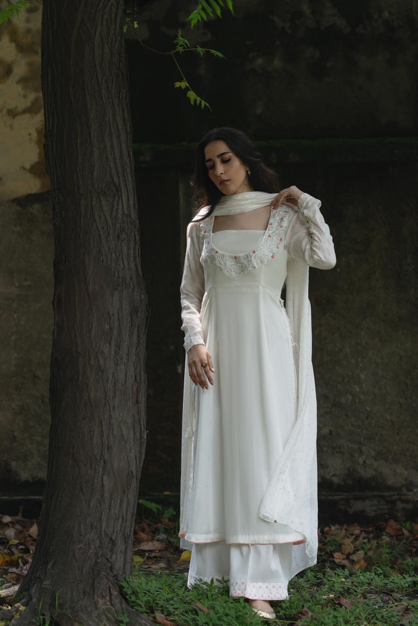 Woman in a white dress standing next to a tree in a natural setting