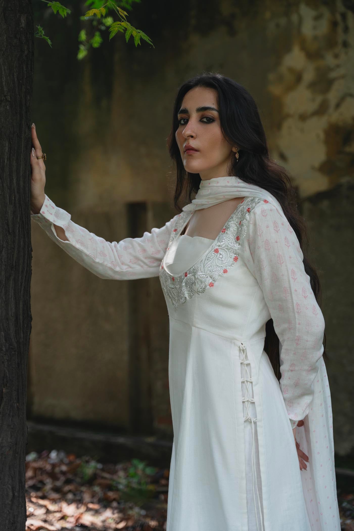 Woman in a white embroidered dress standing next to a tree