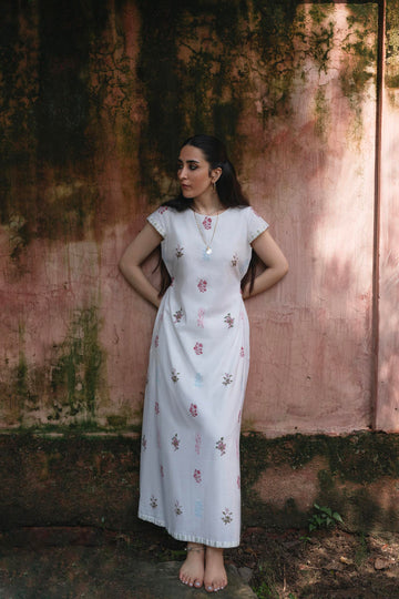 Woman in a white floral dress standing against a textured wall.