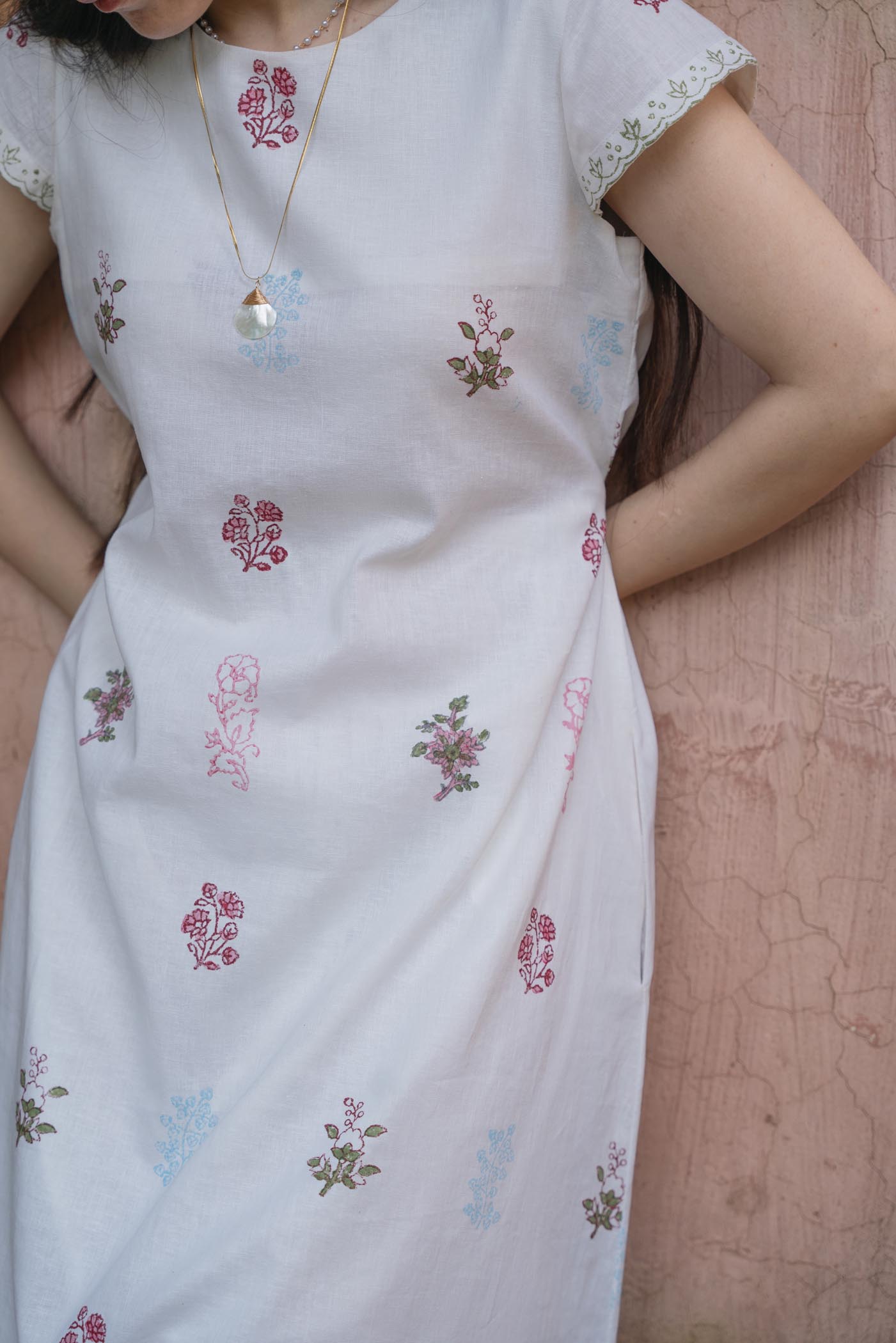 White dress with floral patterns worn by a women against a pink textured background